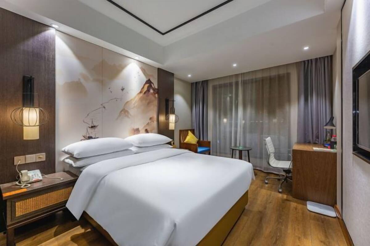 A hotel room with a large bed, a desk, a chair, and a TV.