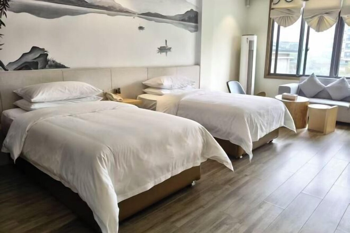 Habitación de hotel con dos camas, un sofá, una mesita y una pared decorada con un cuadro de montañas.
