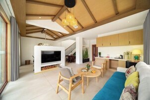 Una sala de estar moderna con televisor, muebles de madera, un sofá y una zona de cocina con armarios y una mesa de comedor.