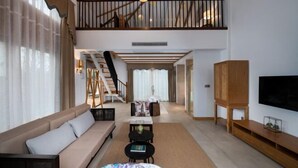 A spacious living area with a high ceiling, a staircase, a sofa, a coffee table, and a TV on the wall. - Venus Resort (Yidu)