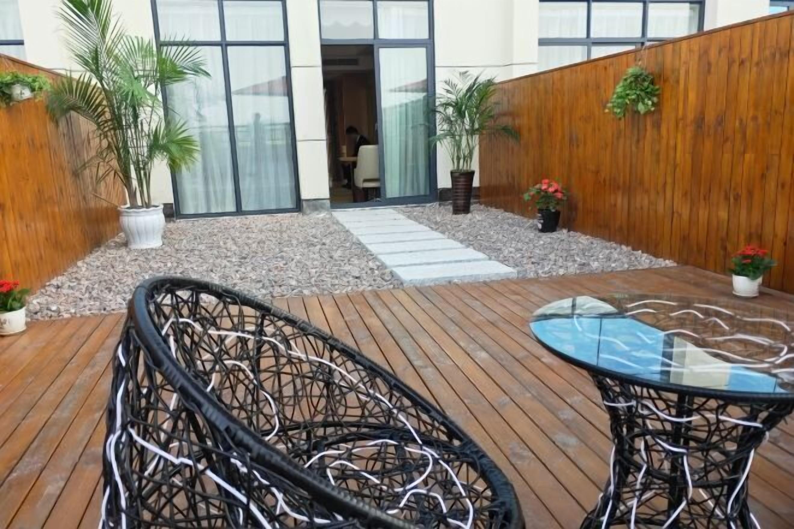 Eine Holzterrasse mit Korbstühlen und einem Glastisch, umgeben von Topfpflanzen und einem Holzzaun.