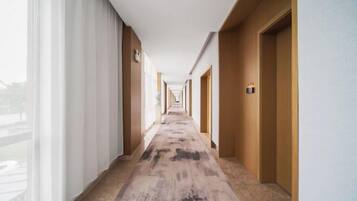 Um corredor de hotel com piso coberto por carpete, portas de madeira e uma janela à esquerda.