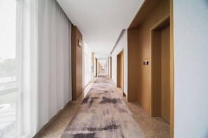 Un pasillo de hotel con piso alfombrado, puertas de madera y una ventana a la izquierda.