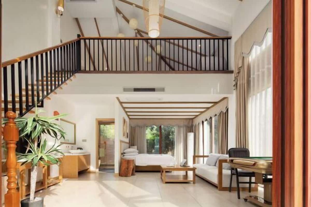 A spacious room with a large bed, a sitting area, and a staircase leading to an upper level.
