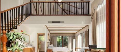 A spacious room with a large bed, a sofa, a desk, and a staircase leading to an upper level.