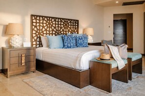 A hotel room with a bed, nightstands, a decorative headboard, and a bench with a hat and bag.