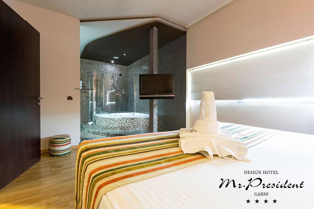 A modern hotel room with a large bed, a TV, a shower area, and a unique wall design.