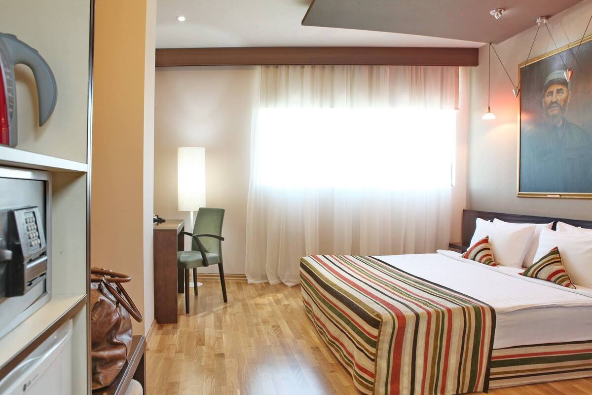 A hotel room with a bed, a desk, a chair, and a large window with curtains.