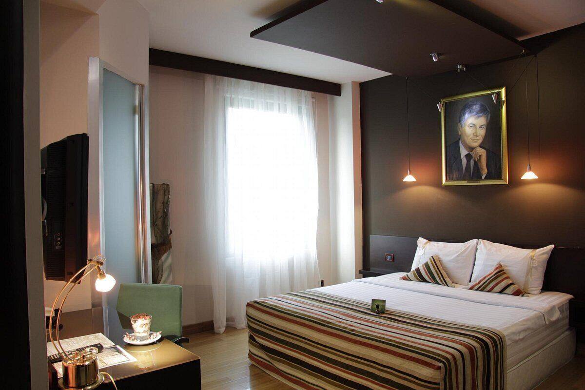 A hotel room with a bed, a desk with a lamp, a chair, a TV, and a window with curtains.
