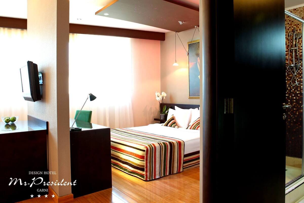 A modern hotel room with a bed, a desk, a TV, and a shower area.