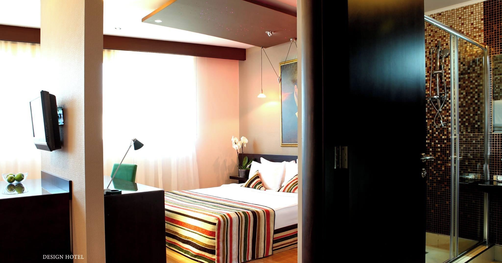 A modern hotel room with a bed, a desk, a TV, and a shower area.