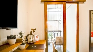 Ein Holztisch mit Blumentöpfen, einem Wasserkocher und einem Schild. Eine Schiebetür führt zu einem Balkon mit einem Stuhl und einem Geländer.