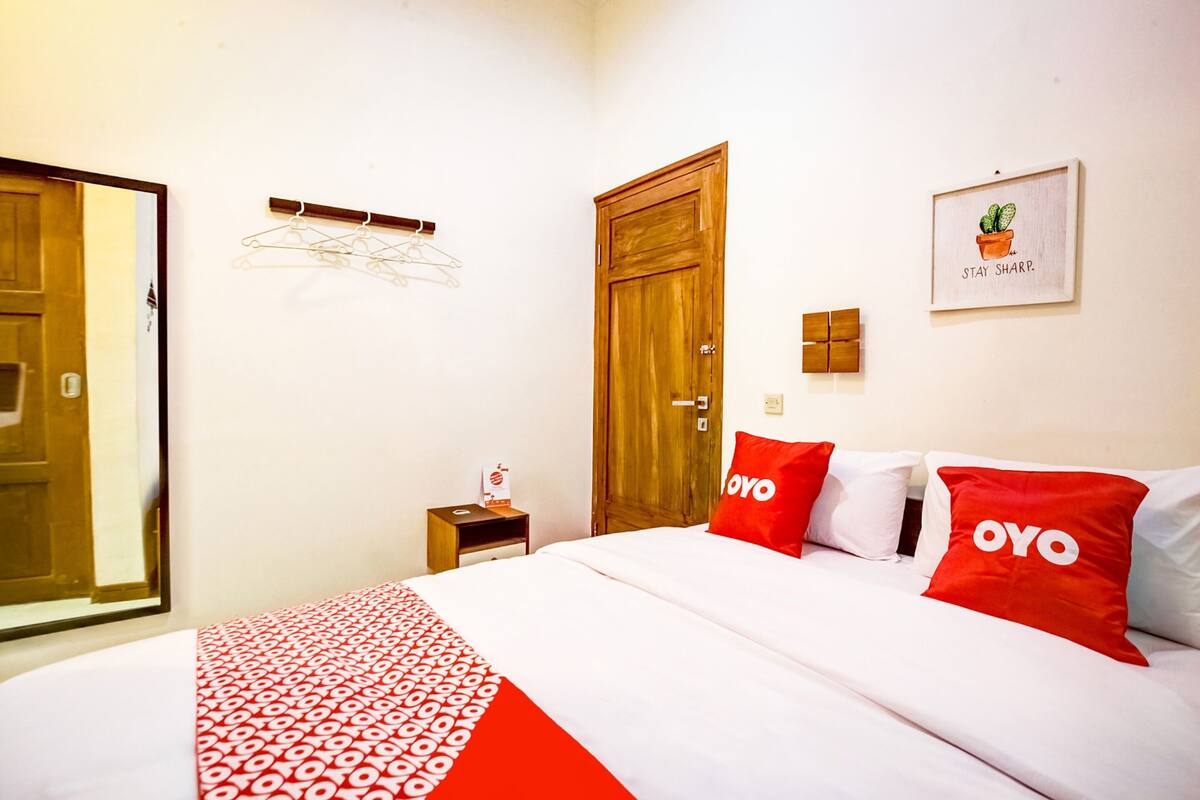 Ein Hotelzimmer mit einem Bett, einem Holzschrank, einem kleinen Nachttisch, einer Wandleuchte und einem gerahmten Bild.