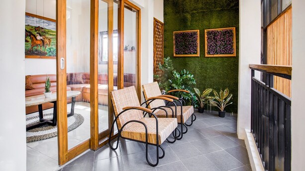 Ein modernes Interieur mit Schiebeglasüren zu einem Balkon, Korbstühle, eine grüne Wand mit gerahmten Bildern und Topfpflanzen.