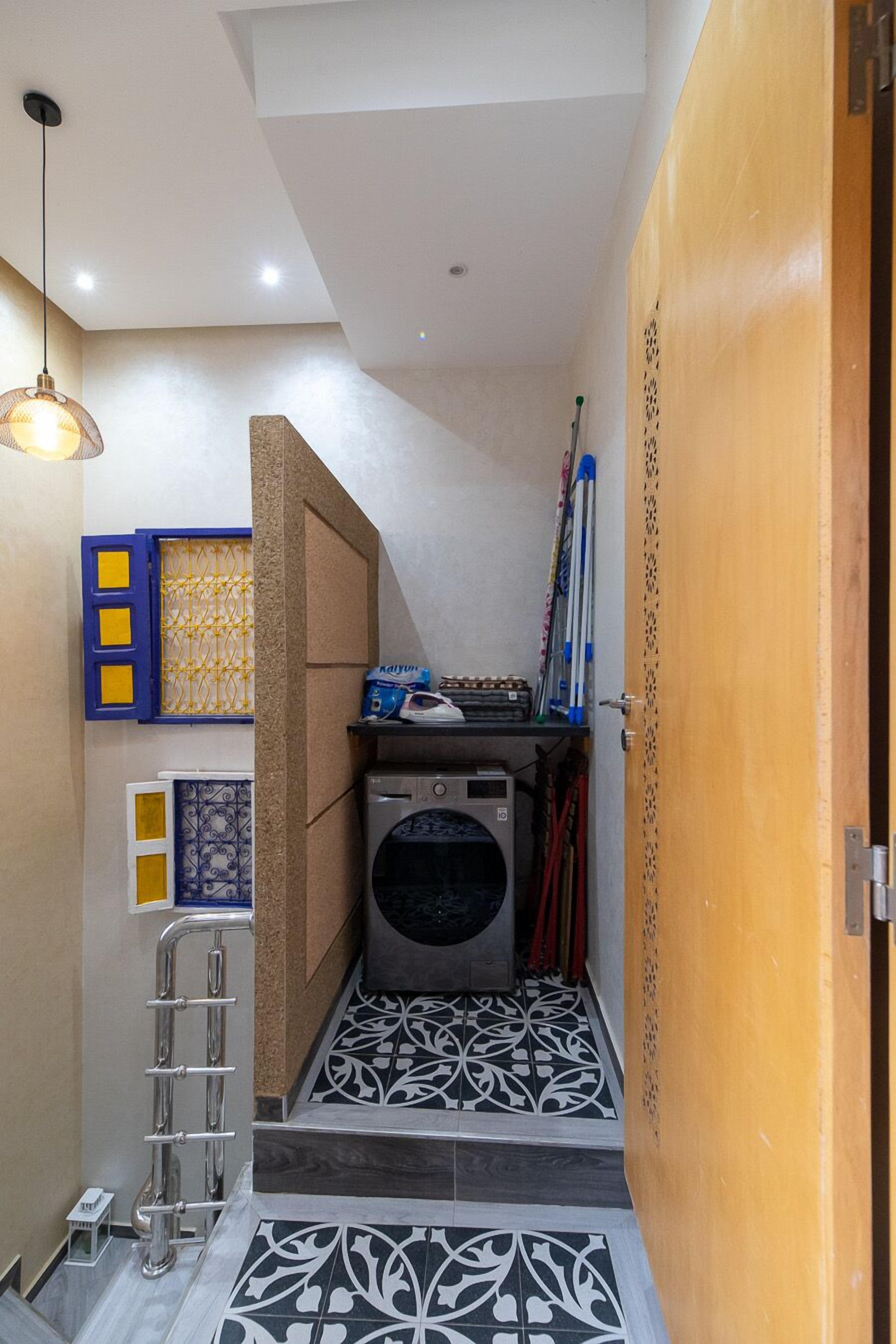 A compact laundry room with a washing machine, a drying rack, and a metal handrail.