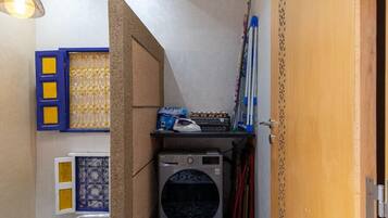 A compact laundry room with a washing machine, a drying rack, and a metal handrail.