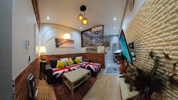 A cozy living room with a sofa, coffee table, and decorative pillows. A flat-screen TV is mounted on the wall, and there is a plant in the corner. - Maison Fifi (Drâa-Tafilalet)