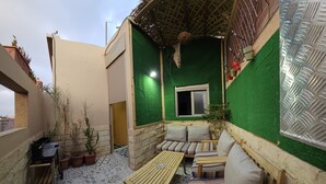 A cozy outdoor seating area with a patterned floor, a wooden table, and cushioned seating. - Maison Fifi (Drâa-Tafilalet)