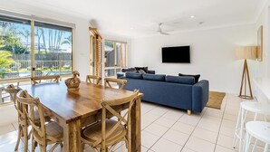 A modern living room with a wooden dining table, blue sofa, and a flat-screen TV mounted on the wall.