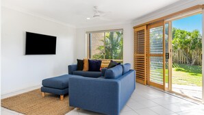 A modern living room with a blue sofa, a flat-screen TV, and a large sliding glass door leading to a garden.