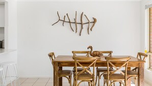 A dining area with a wooden table and chairs, a wall-mounted branch sculpture, and a window with blinds.