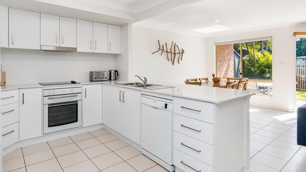 A modern kitchen with white cabinetry, a built-in oven, a dishwasher, and a large island with a sink.