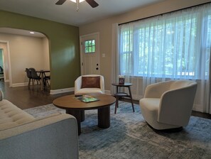 Una sala de estar con una mesa de centro redonda, un sillón blanco y un comedor con sillas.