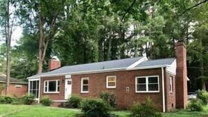 A single-story brick house with a front porch, a chimney, and a small front yard.