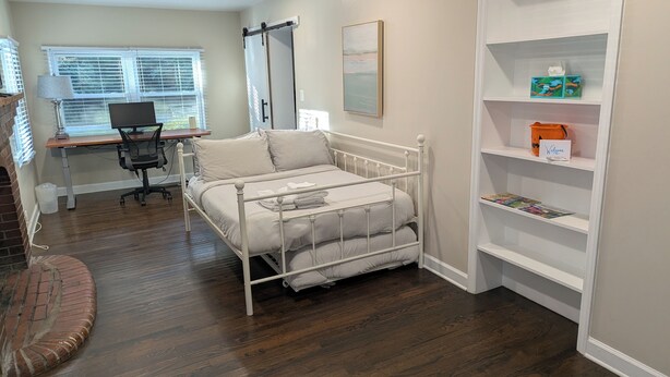 A bedroom with a bed, a desk, a chair, a bookshelf, and a window with blinds.