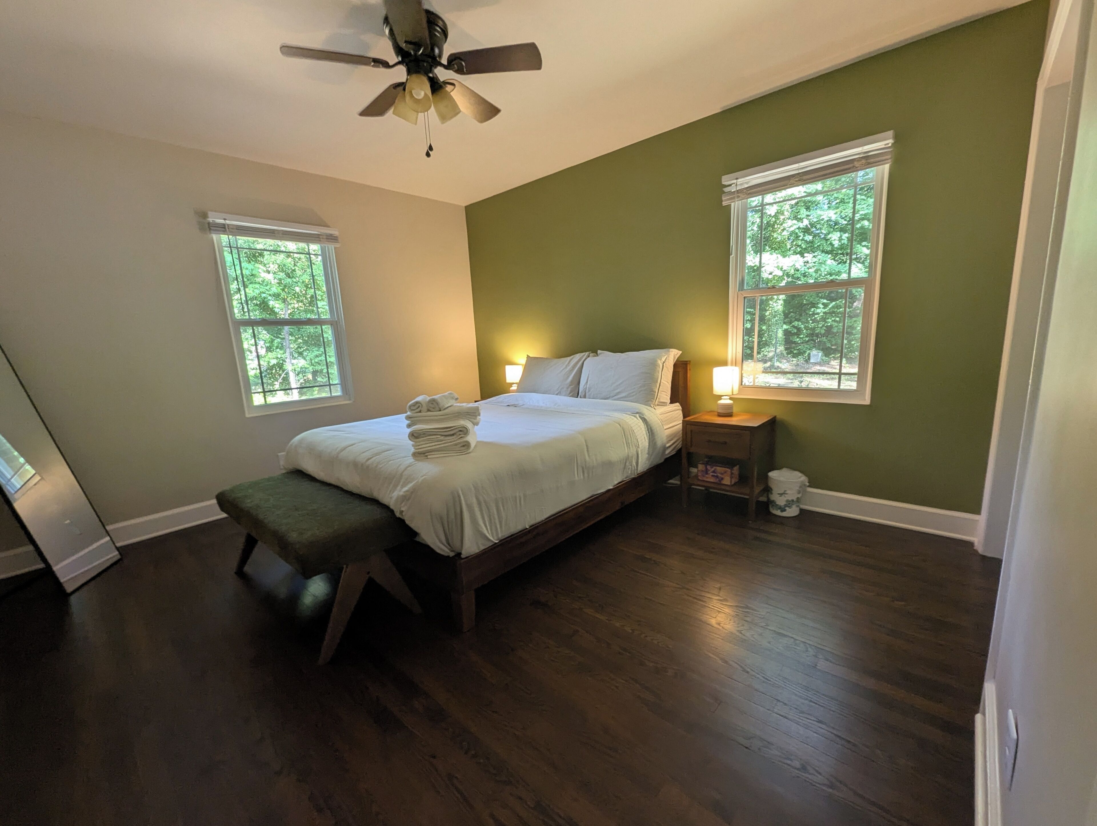 A bedroom with a bed, two windows, a nightstand, and a ceiling fan.