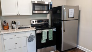 A kitchen with white cabinets, a stainless steel microwave, a black stove, a stainless steel refrigerator, and a granite countertop.