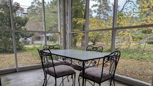 A covered patio with a table and chairs, large windows, and a view of trees and a road.