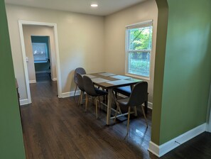 Un comedor con una mesa y sillas, una ventana con vistas a zonas verdes y un pasillo que lleva a otra habitación.