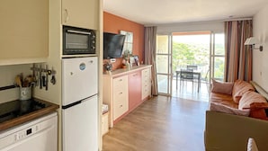 A compact kitchen with a microwave, a small refrigerator, and a sink. There is a dining area with a table and chairs, and a balcony with a view. - Duplex with terrace and solarium, pool access and parking included (Saint-Raphaël)