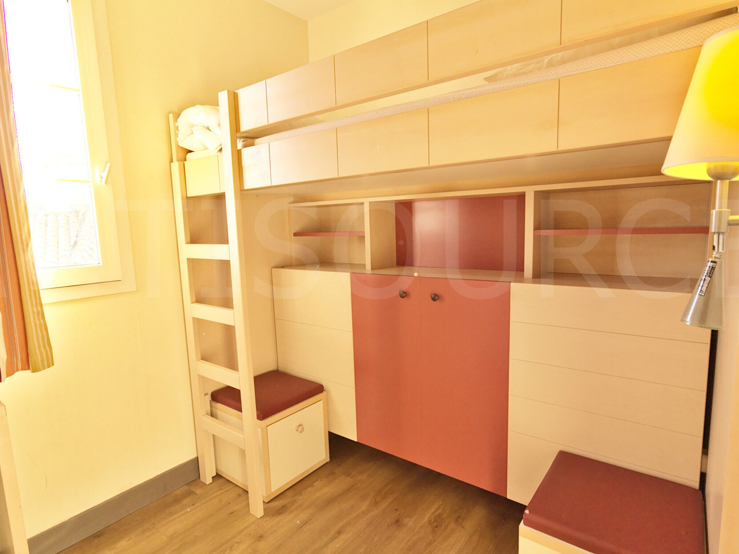 A bunk bed with a desk and drawers, a small ladder, and a lamp.