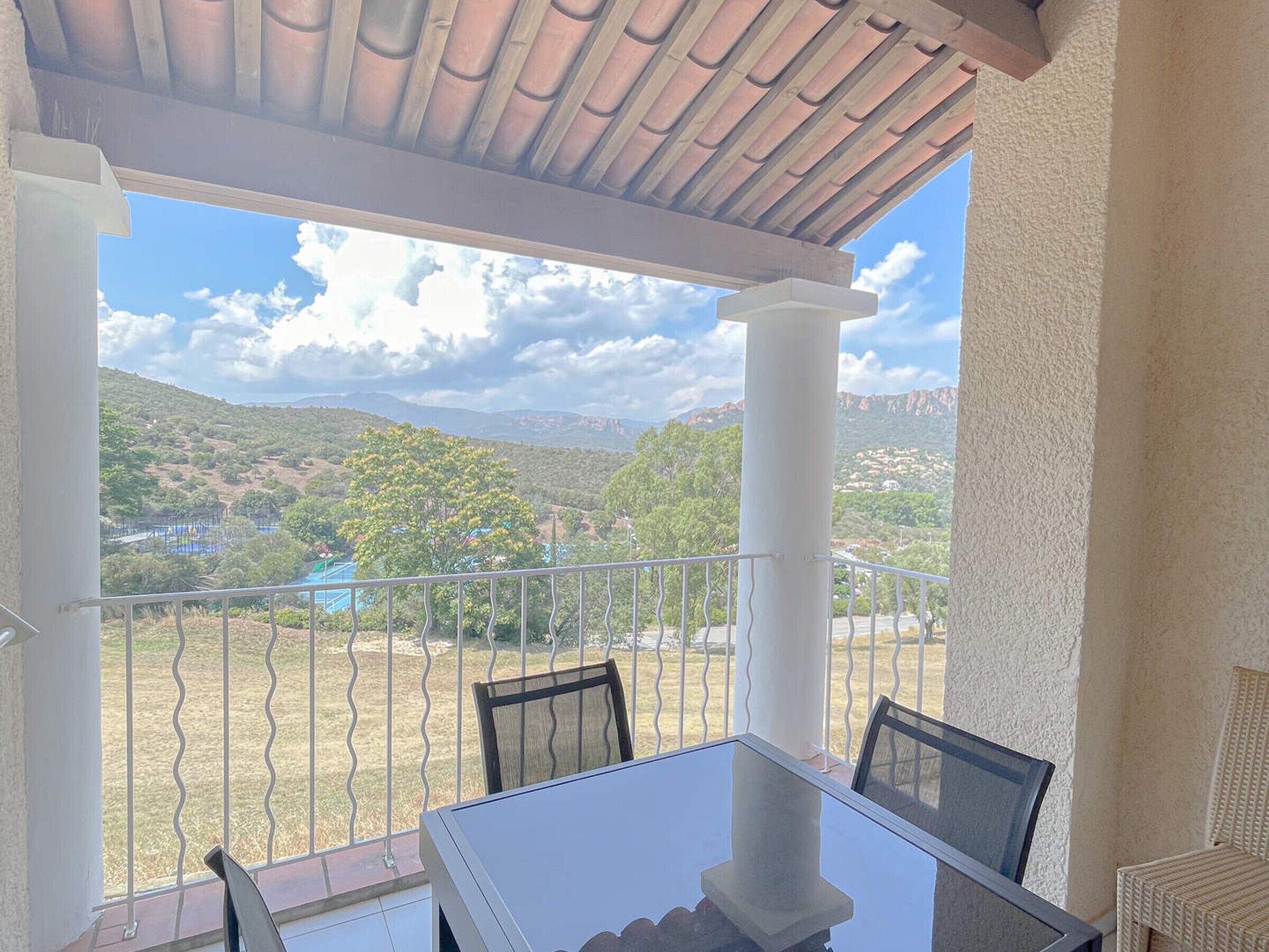 A covered outdoor seating area with a table and chairs, overlooking a mountainous landscape.