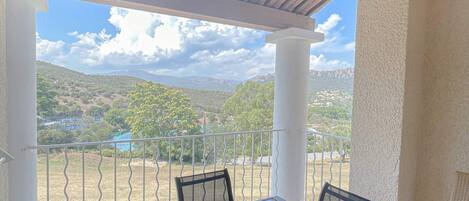 A covered outdoor seating area with a table and chairs, overlooking a mountainous landscape.