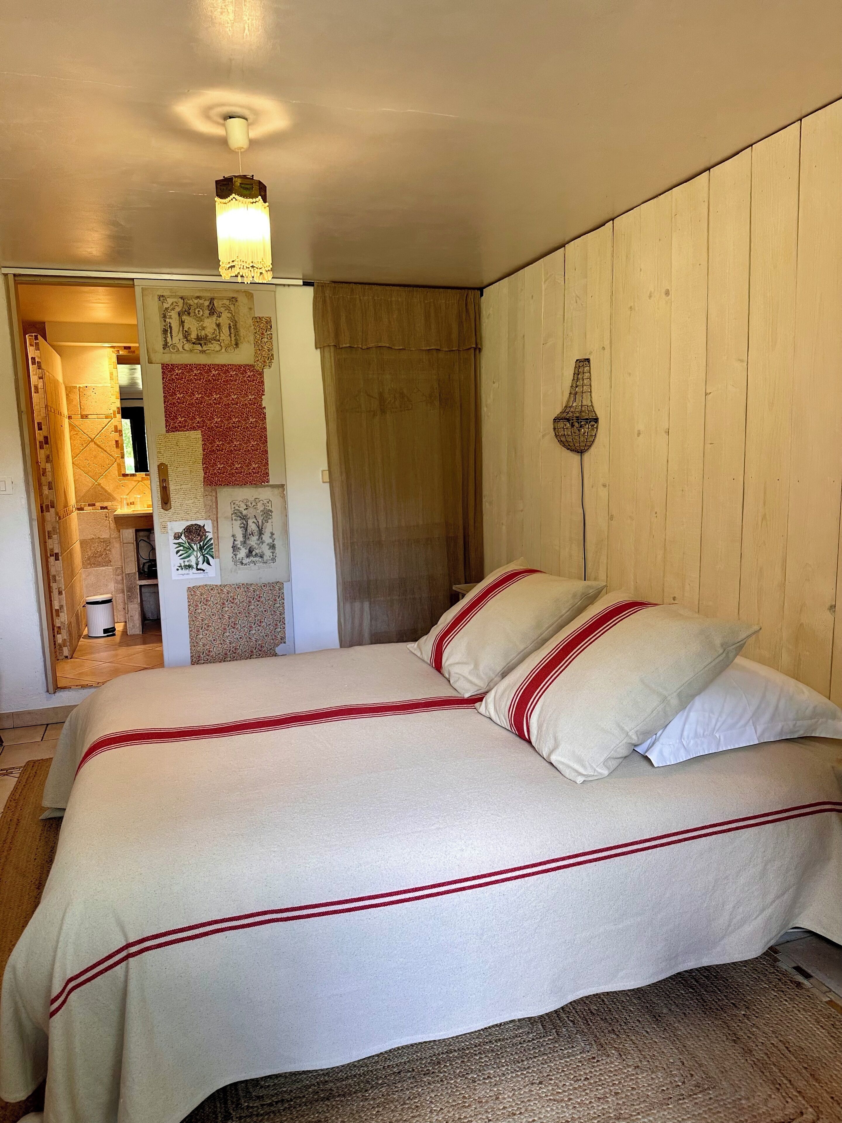 A bedroom with a bed, a wooden headboard, a wall-mounted lamp, and a door leading to a bathroom.