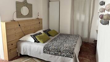 Ein Schlafzimmer mit Holzkopfstütze, einem Bett mit gemusterten Betttextilien, einem Spiegel, einem Heizkörper und einem Vorhang.