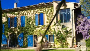 A traditional house with a tiled roof, blue shutters, and a garden with a bench. - Bergerie de Beaudine (Forcalquier)