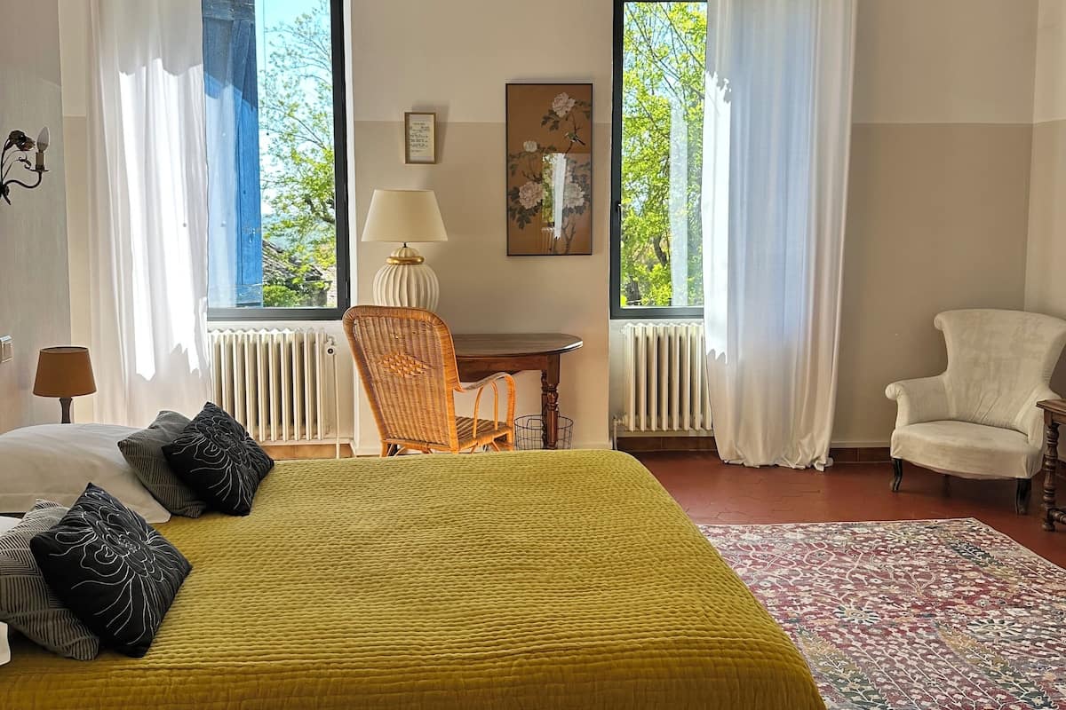 A bedroom with a bed, two chairs, a table, and a window with curtains.