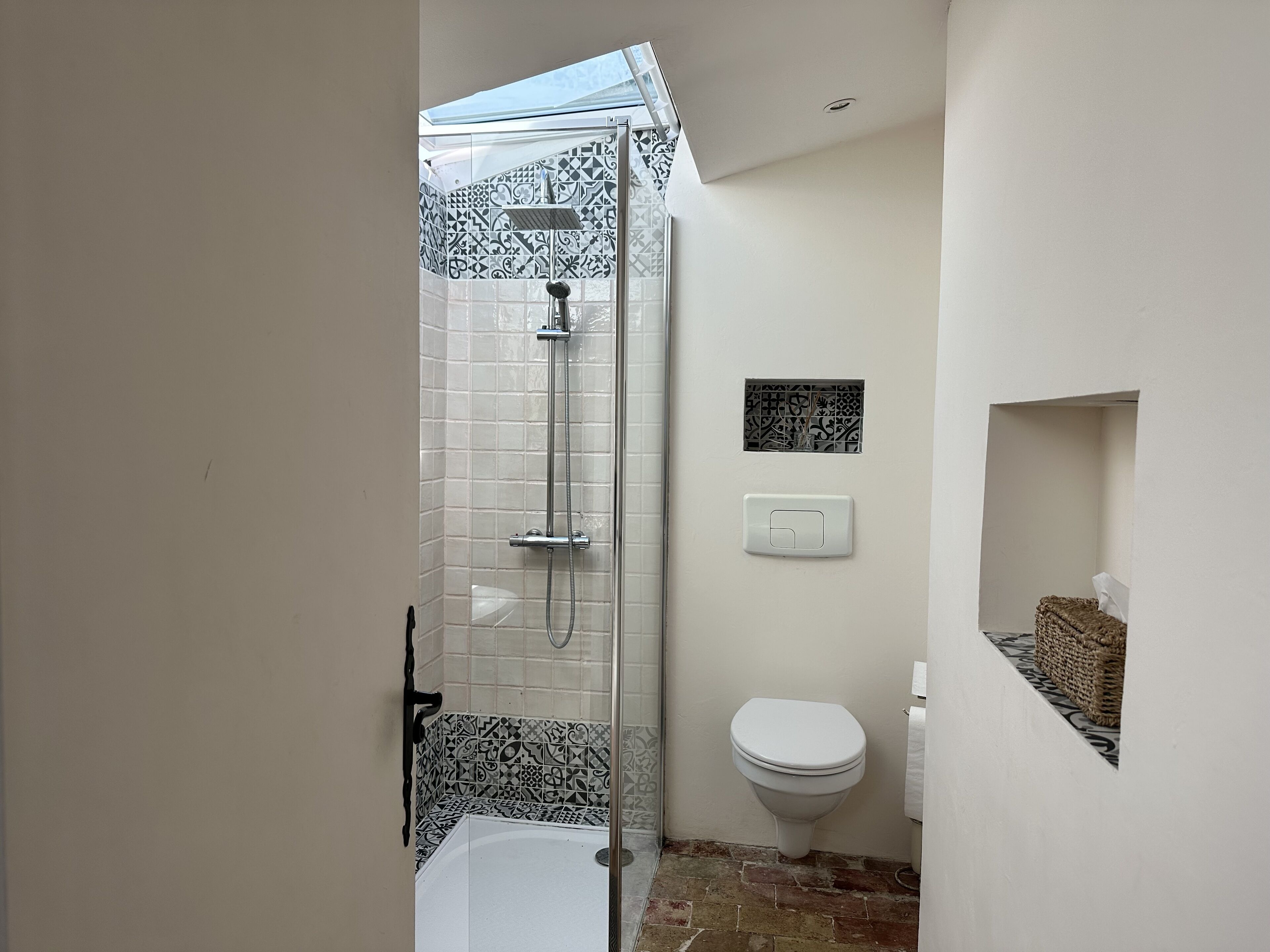 A bathroom with a shower, toilet, and a small shelf with a basket.