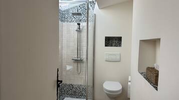 A bathroom with a shower, toilet, and a small shelf with a basket.