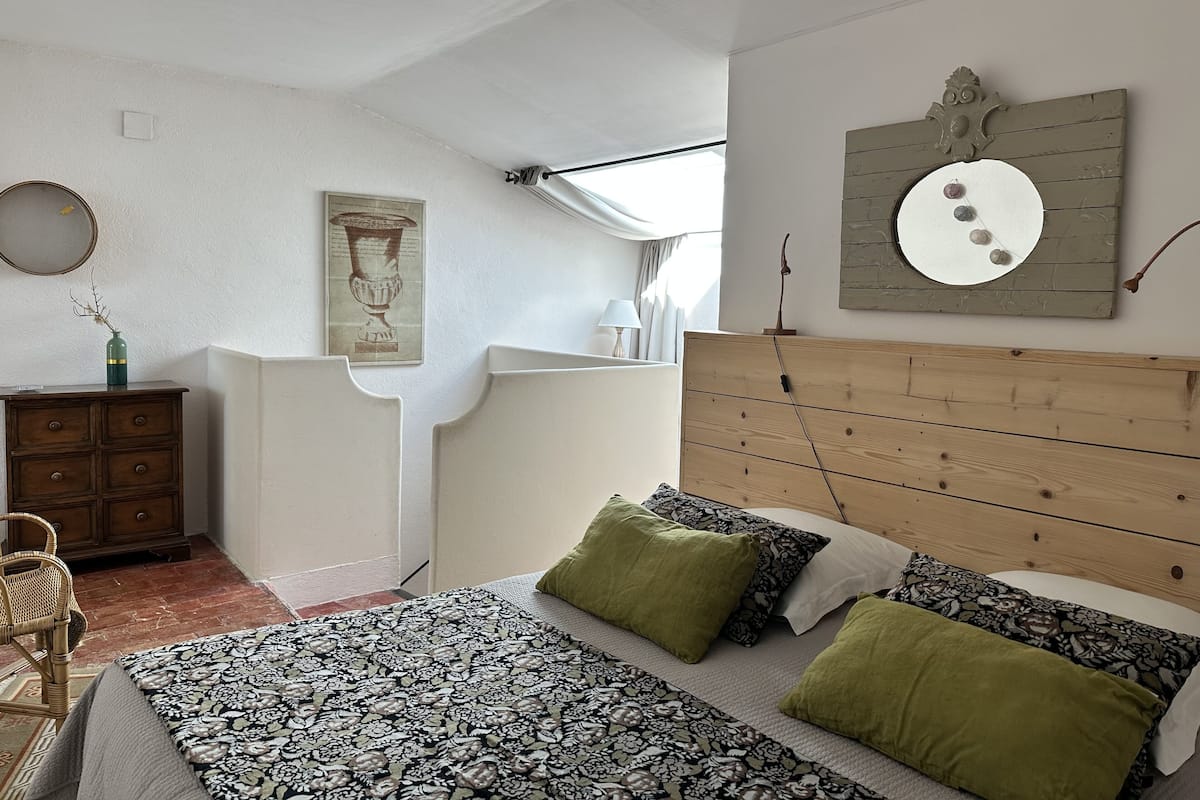 A bedroom with a wooden headboard, a patterned bedspread, and a green pillow.