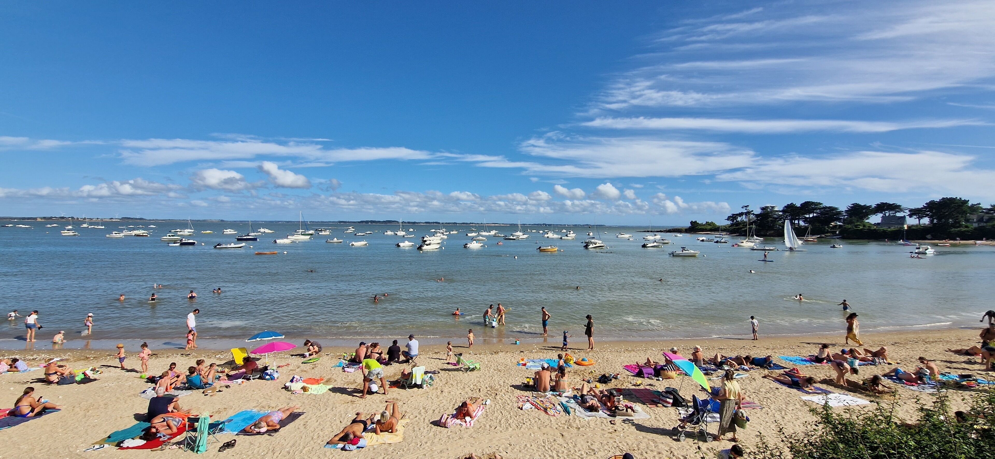 Una spiaggia con persone che prendono il sole e nuotano, e numerose imbarcazioni in acqua.