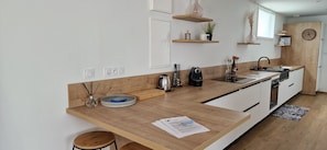 A modern kitchen with wooden countertops, white cabinets, and a built-in oven. There are hanging shelves with decorative items and a clock on the wall.