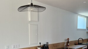Une cuisine moderne avec un plan de travail en bois, deux tabourets, un luminaire suspendu et une fenêtre.