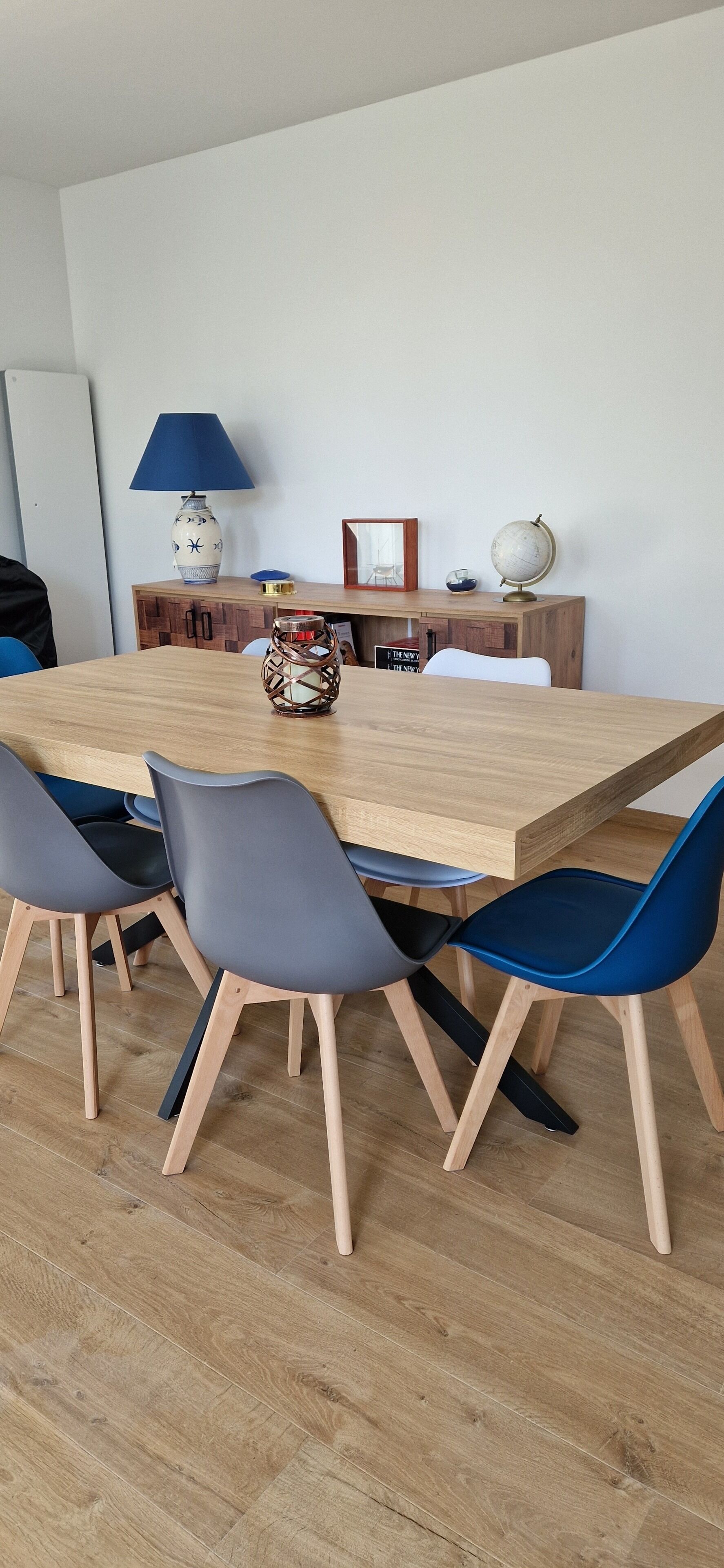 A dining area with a wooden table, blue and gray chairs, a lamp, a globe, and a framed picture on a wooden cabinet.