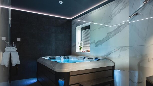 A modern bathroom with a marble wall, a large bathtub, and a window with blinds. - La Siesta (Markovci)