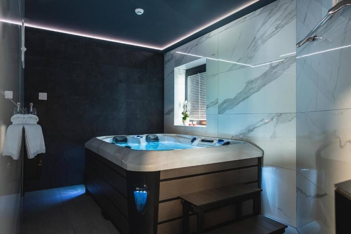 A modern bathroom with a marble wall, a large bathtub, and a window with blinds.